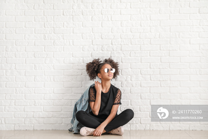 Stylish African-American girl in jeans near white brick wall