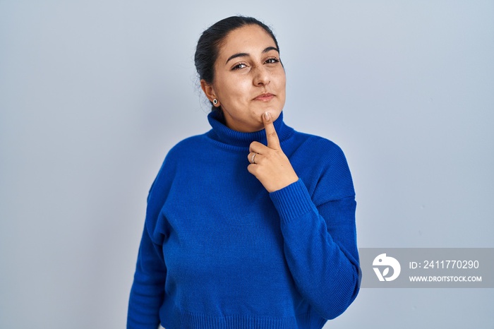 Young hispanic woman standing over isolated background thinking concentrated about doubt with finger on chin and looking up wondering