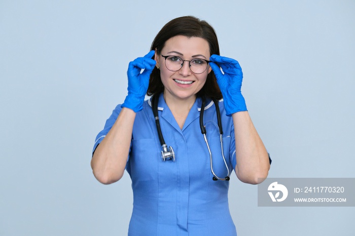 Portrait of nurse woman in blue uniform, stethoscope, gloves, holding glasses