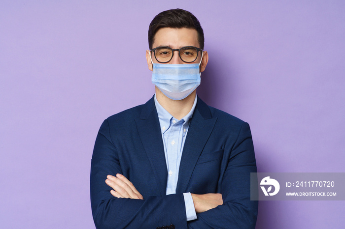 Young business man wearing glasses and medical mask, standing with crossed arms isolated on purple background