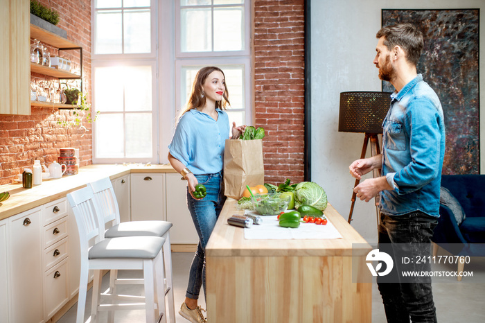 Young couple of vegetarians unpacking shopping back with fresh green product on the kitchen at home