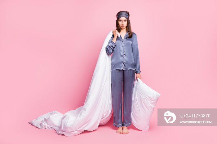 Full length photo portrait of upset girl holding blanket and pillow in hands isolated on pastel pink colored background