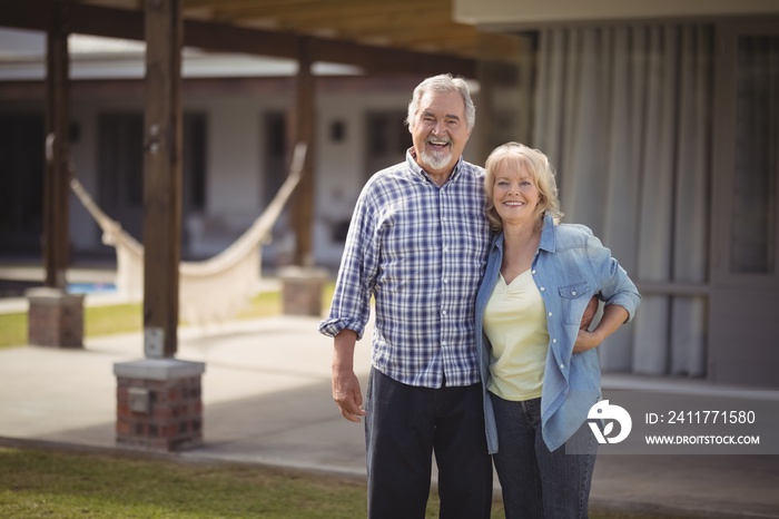 Senior couple smiling while standing outside their house.