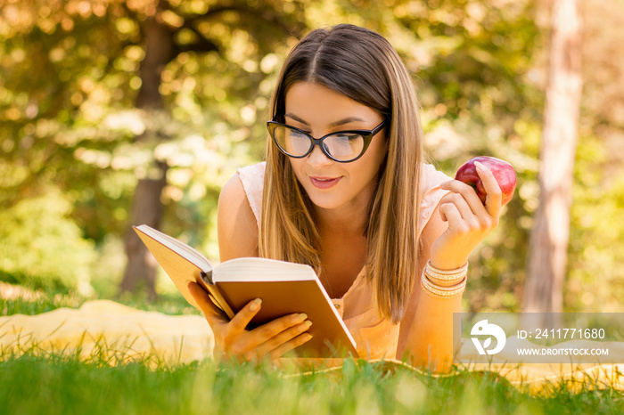 outside portrait of young beautiful woman with apple reading book in park