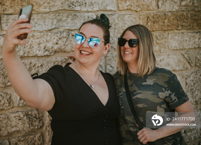 closeup of 2 women taking a selfie against a brick wall