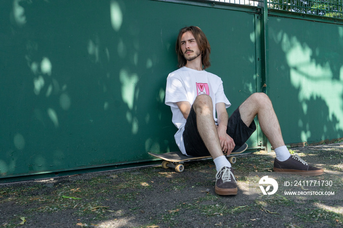 Young man sitting on skateboard in park