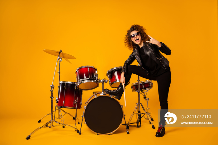 Full body photo of redhair lady stand leg on drum instruments show horns fingers crazy rocker concert performance photographing wear leather jacket sun glasses isolated yellow background