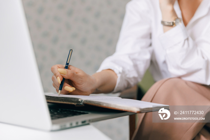 Closeup woman psychotherapist is holding notebook and making notes during online therapy session, background internet laptop with web call