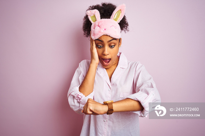 Young african american woman wearing pajama and mask over isolated pink background Looking at the watch time worried, afraid of getting late