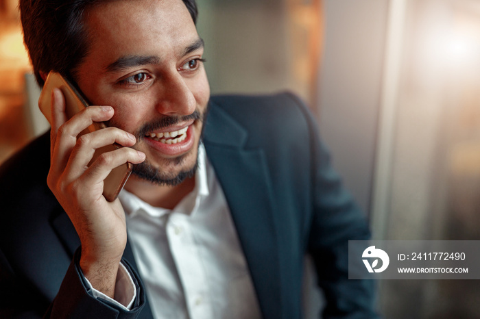 Close up of smiling indian businessman talking by phone with client. Blurred background