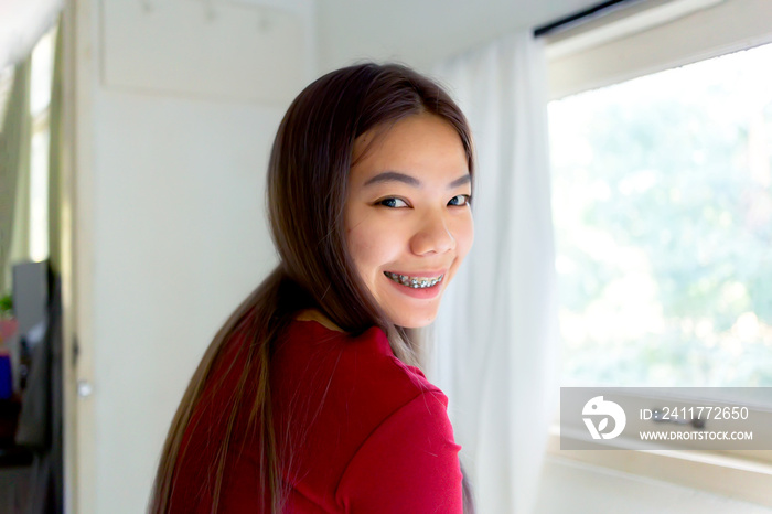 Asian woman in a red shirt smiling while cooking in the kitchen. An Asian teenager who braces her teeth, smiles and looks at the camera.