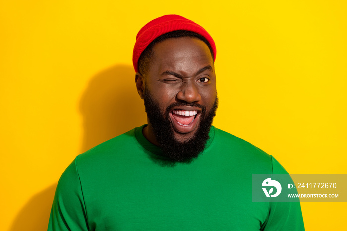 Portrait of attractive flirty cool cheerful funny guy wearing cap winking isolated over vivid yellow color background