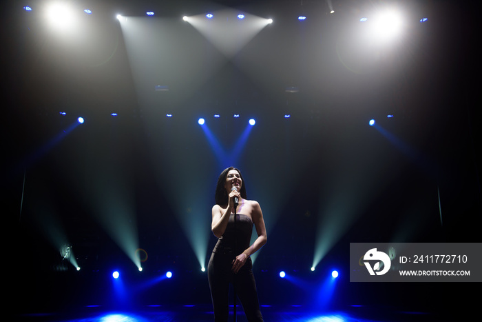 Singer perform on stage of nightclub in front of bright screen. Dark background, smoke, concert spotlights