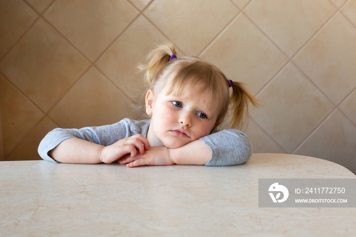 Beautiful little girl kid sad or bored sits by the table