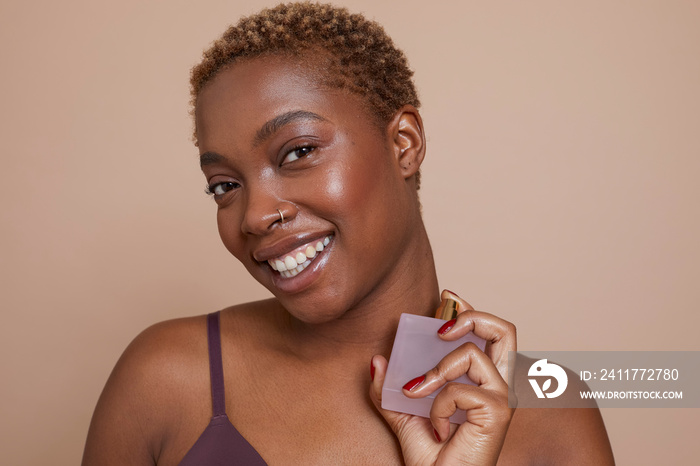 Studio portrait of smiling woman spraying perfume on neck