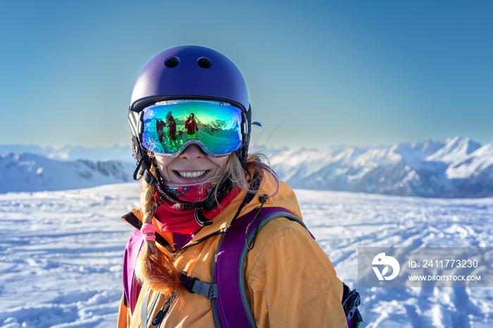 portrait of young woman in a bright jacket and blue helmet with a bright ski mask with reflection of winter ski resort