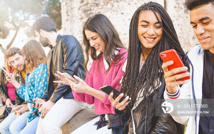 Multiracial group of teenagers have fun playing happily with smartphones. Use by millennials of cell phones and social applications. Focus on the face of a beauty mixed race girl with dreadlocks