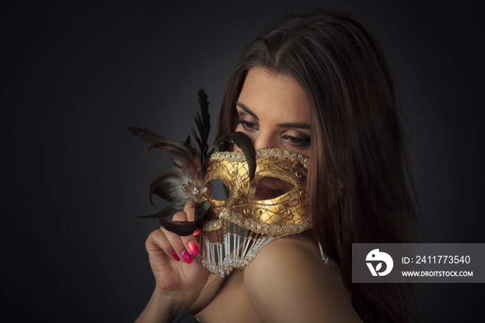 Young attractive woman in a black dress with golden carnival mask.