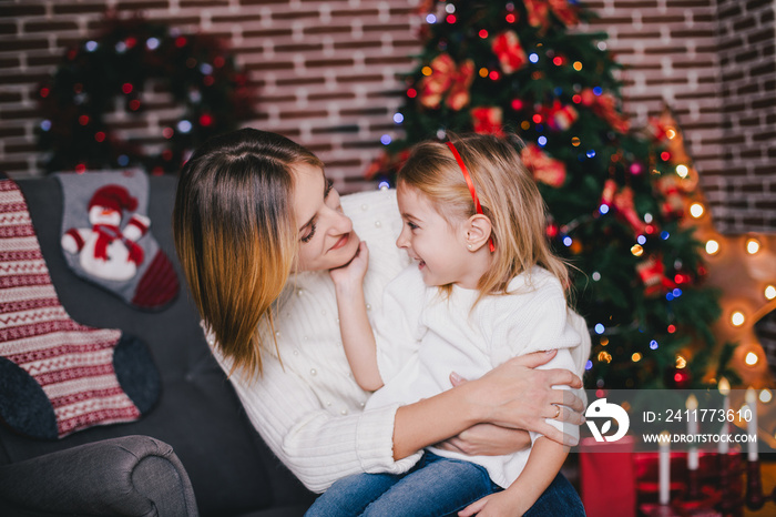 Happy beautiful mother and her little daughter posing near Christmas tree in a holiday interior