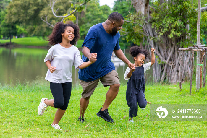 Happy mixed race family in park. African father carrying and holding hand two little daughter walking together in garden. Dad and cute child girl kid enjoy and having fun outdoor lifestyle activity