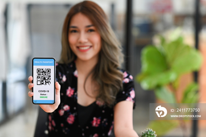 Smiling asian woman showing smart phone with health passport of vaccination certification on screen.