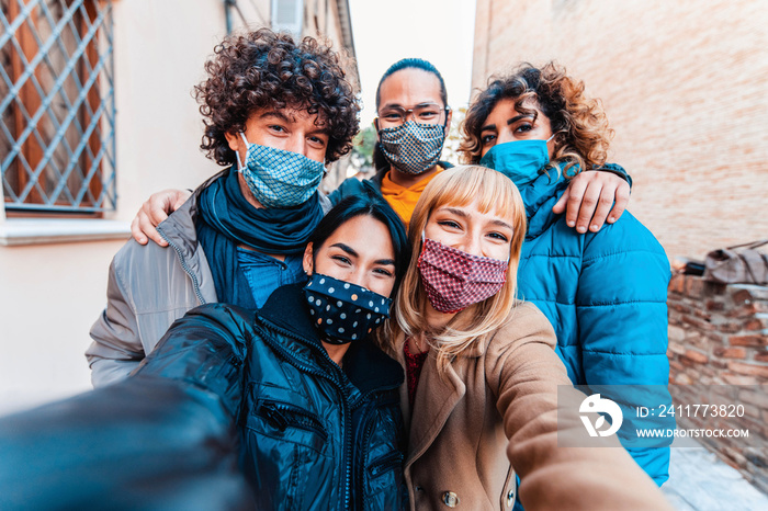 Friends covered by facemasks taking a selfie outside in the city - New normal lifestyle concept with young people having fun together outdoors on vacation