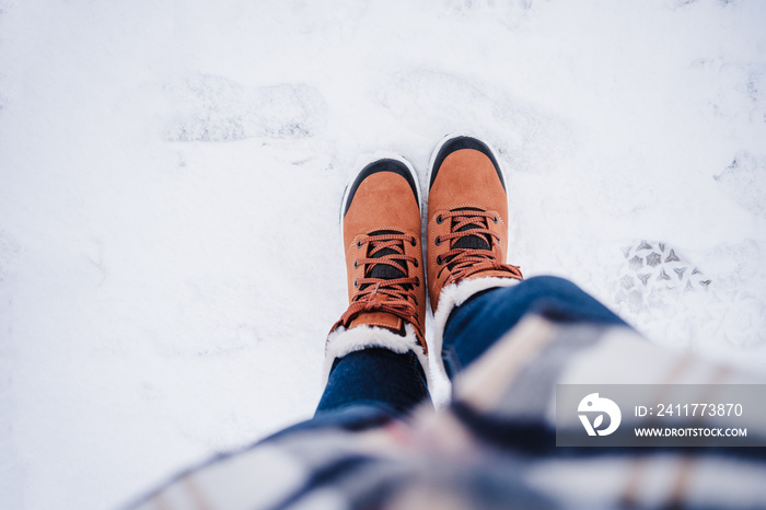 top view of unrecognizable female feet boots standing on snowy landscape during winter. hiking concept