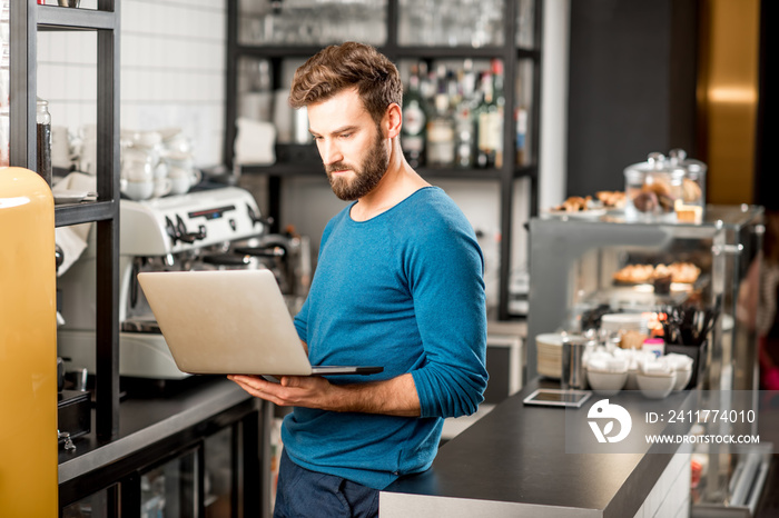 Handsome man in blue sweater working with laptop at the bar of the modern cafe interior