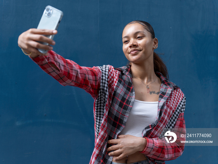 Young woman taking selfie against blue wall