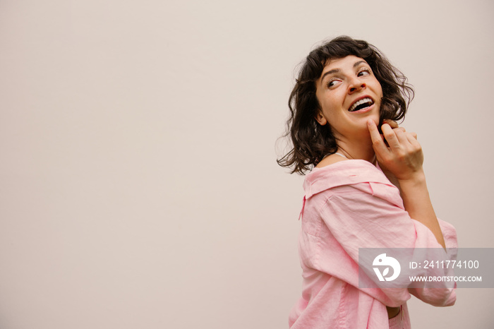 Cheerful young caucasian woman looking back standing on white background with space for text. Brunette wears pink shirt in warm season. Positive emotions concept