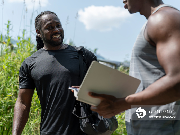 Two men planning workout on digital tablet