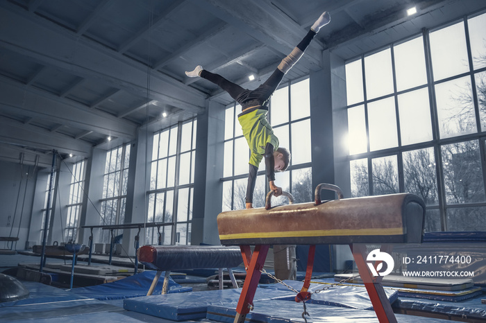 Champion. Little male gymnast training in gym, flexible and active. Caucasian boy, athlete in sportswear practicing in exercises for strength, balance. Movement, action, motion, dynamic concept.