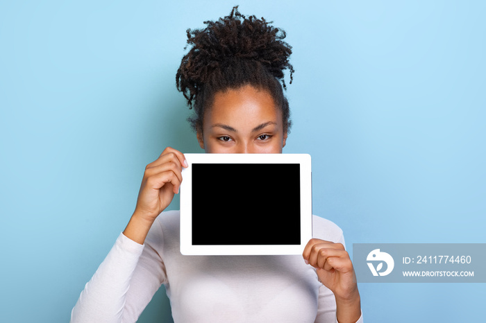 Mockup image of black empty blank screen of tablet in the female hand, peeking from behind tablet over blue background