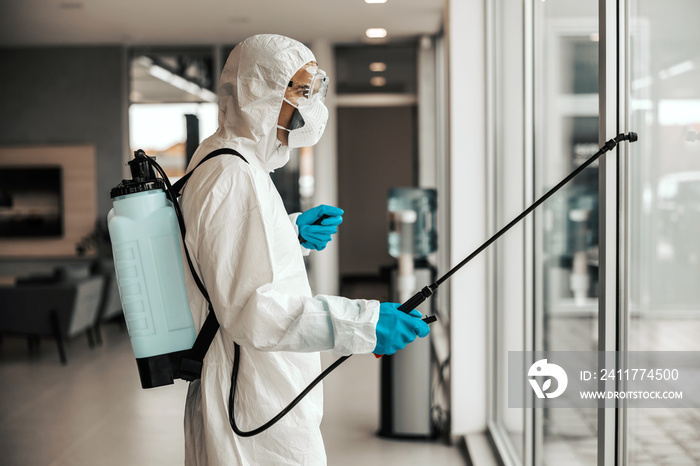 Coronavirus outbreak situation. A male specialist in a special protective suit and sprayer refreshes and cleans the door and windows. Social distancing,keep distance in public to protect from COVID-19