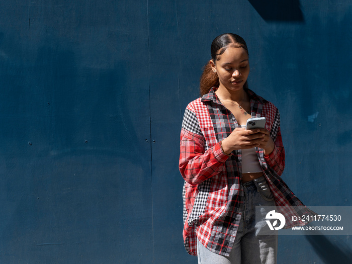 Young woman standing with smart phone against blue wall