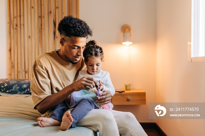 Young dad painting his daughter’s nails with nail polish at home