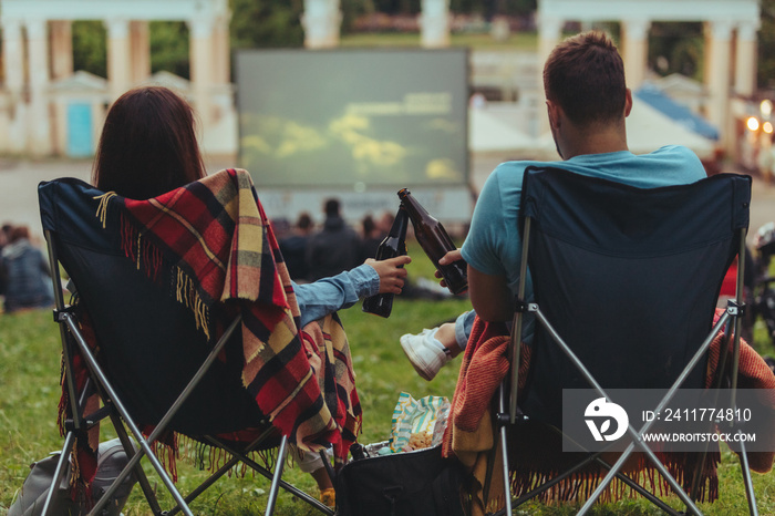 couple sitting in camp-chairs in city park looking movie outdoors at open air cinema