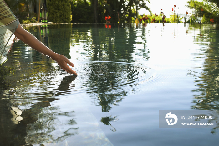 Woman’s hand touching water of outdoor swimming pool