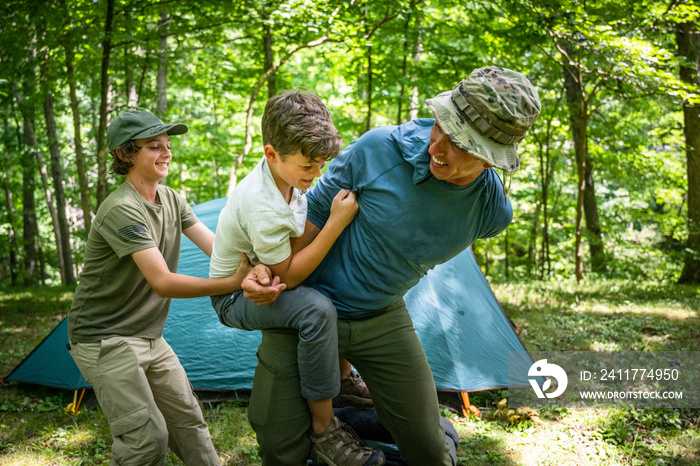 Air Force service member sets up a tent with his sons on  a backpacking trip.