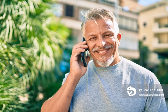 Middle age hispanic grey-haired man smiling happy talking on the smartphone at the park.