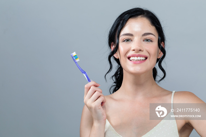 Young woman holding a toothbrush on a gray background