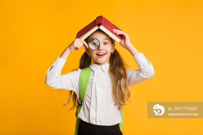 Cute Curious Schoolgirl Looking Through Magnifier Covering Head With Book