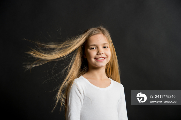 Little girl smile with long blond hair on black background. Happy child with fashion hairstyle. Beauty kid smiling with adorable look. Beauty salon. In this salon we love hair