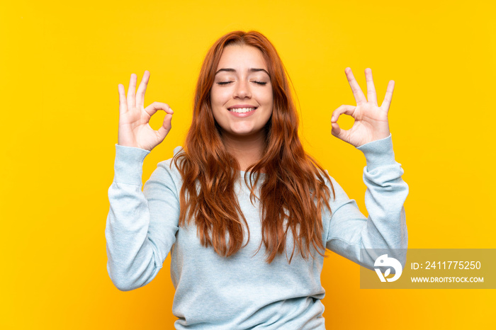 Teenager redhead girl over isolated yellow background in zen pose