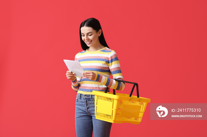 Young woman with shopping basket and list of products on color background