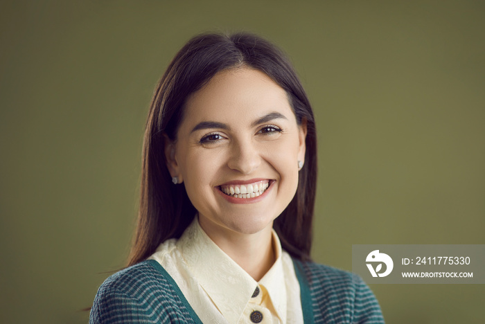 Studio close up portrait of happy smiling good looking woman. Closeup headshot of cheerful confident young girl in smart casual outfit, with pretty face and charming natural smile on green background