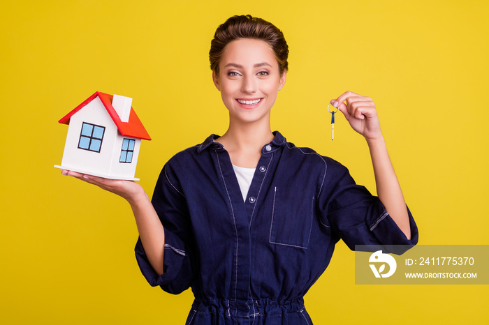 Portrait of attractive cheerful girl holding in hands house key flat isolated over vibrant yellow color background