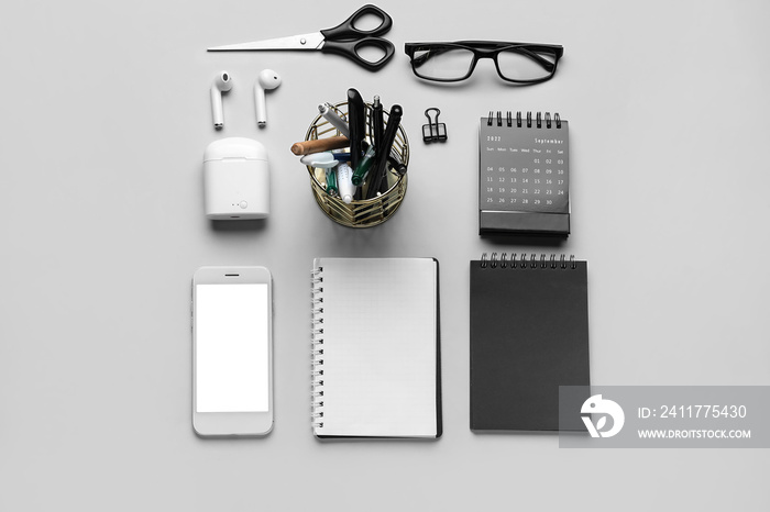 Set of stationery with eyeglasses, mobile phone and earphones on light background