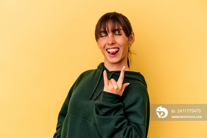 Young Argentinian woman isolated on yellow background showing rock gesture with fingers