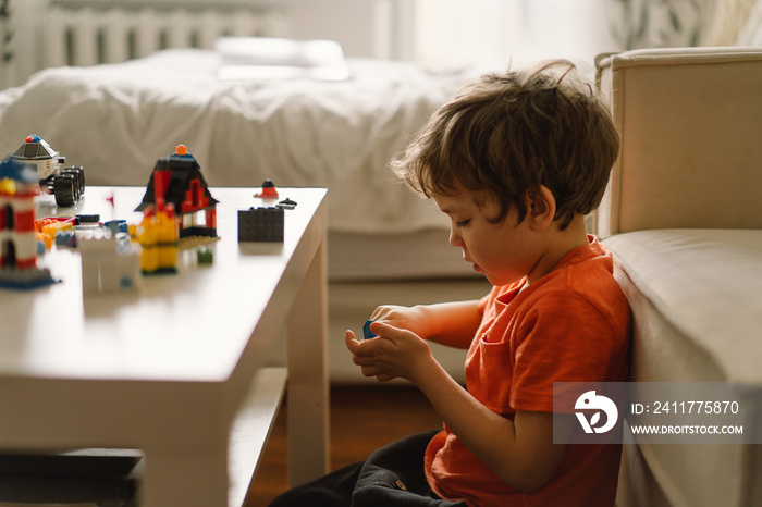 Cute boy is playing constructor at home. Kid playing block toys in home at nursery. Toddler having fun and building out of bright constructor bricks. Development and Construction Concept